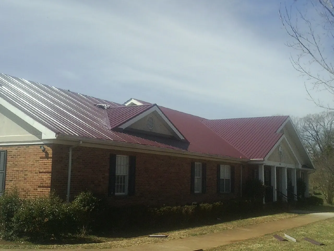 Red metal roof with gabled entries on a long brick building, from a Hail Damage Roof Repair job in Sparta