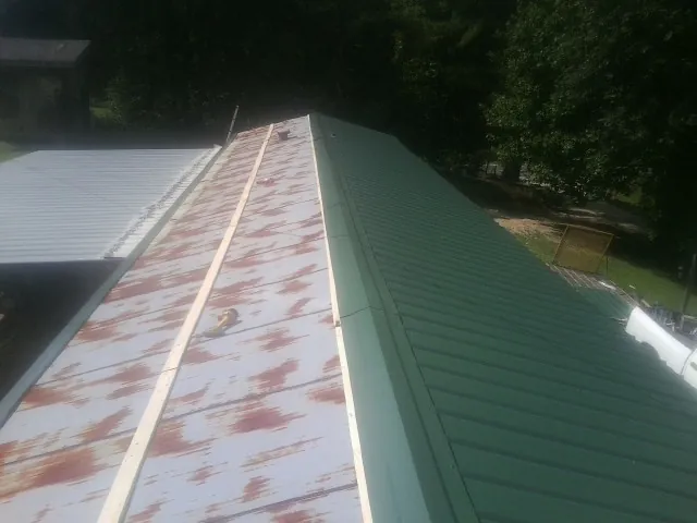 Old rusted panels beside newly installed green metal roofing — Wind Damage Roof Repair by Roofing Brothers in Sparta