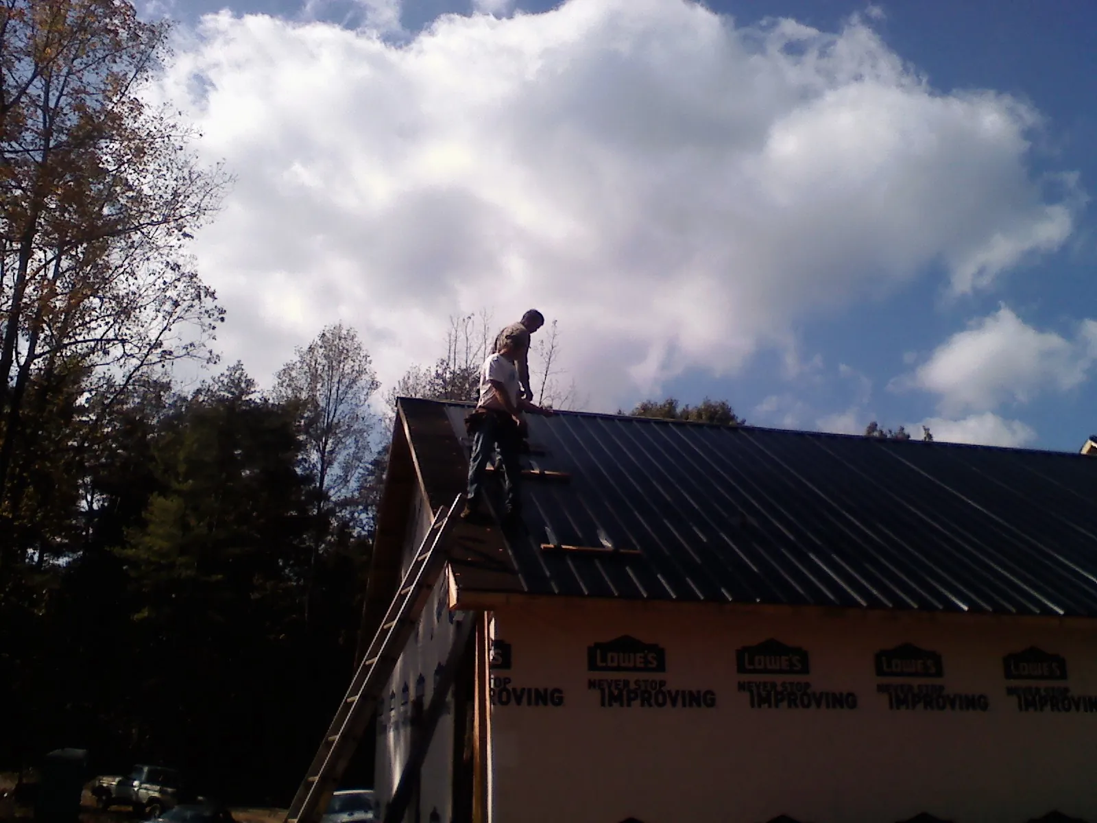 Roofer fastening dark metal panels high against a cloudy sky, from a Roof Inspection job in Sparta